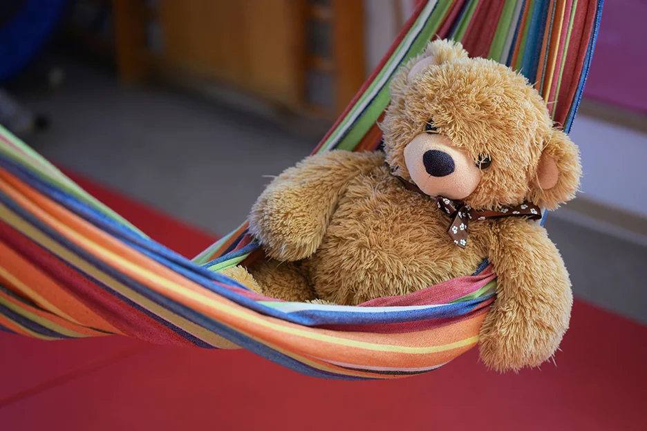 Ein brauner Teddibär liegt in einer bunt gestreiften Hängematte